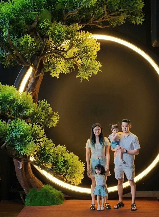 Family of four posing in front of a decorative circular light with plants around.